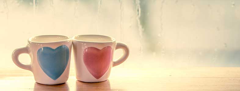 love during the coronavirus 2 heart mugs on table with rain on window in background.