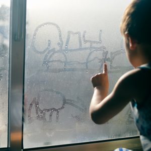 young child playing with condensation on the window
