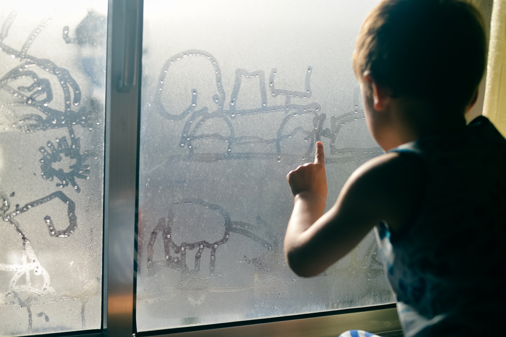 young child playing with condensation on the window