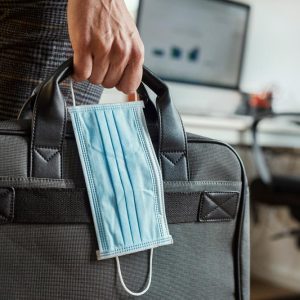 closeup of a young man in an office holding a briefcase and a surgical mask in his hand