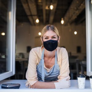 Woman with face mask serving coffee through window, shop open after lockdown.