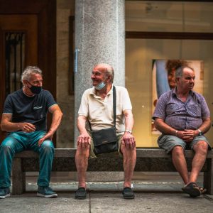 three elderly men sitting on a bench with face masks