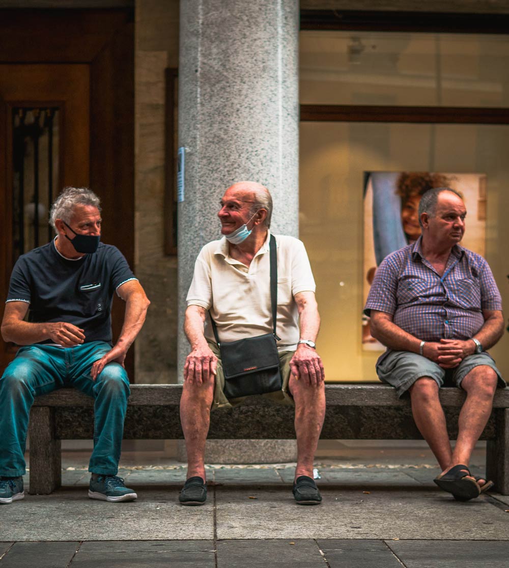 three elderly men sitting on a bench with face masks