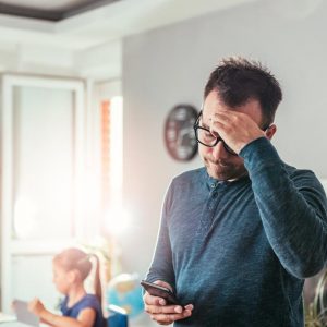 Worried father looking at smart phone and holding hand on forehead with stress