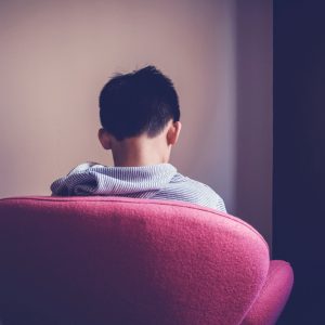 Sad preteen boy sitting alone in chair facing wall